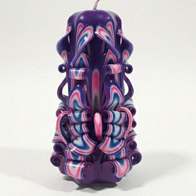 Vela artesanal tallada a mano en tonos púrpura y rosa con diseño ornamental